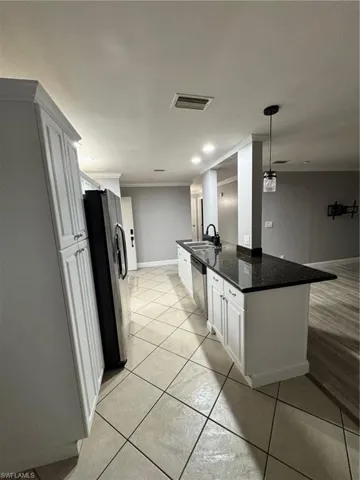 Kitchen featuring white cabinetry, refrigerator, dark stone counters, decorative light fixtures, and a center island with sink