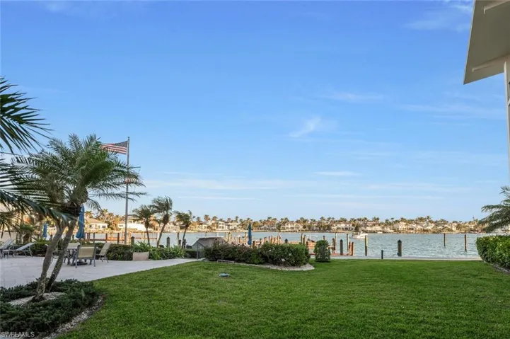View of green lawn with a dock, a water view, and a patio area