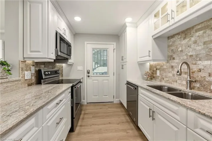Kitchen featuring appliances with stainless steel finishes, white cabinetry, light stone countertops, light wood-style flooring, and recessed lighting