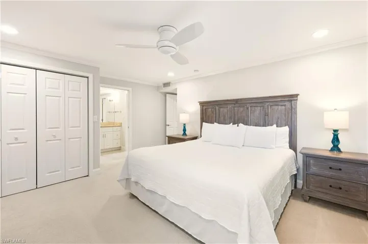 Bedroom with ornamental molding,             ceiling fan, light colored carpet, connected bathroom, and a closet