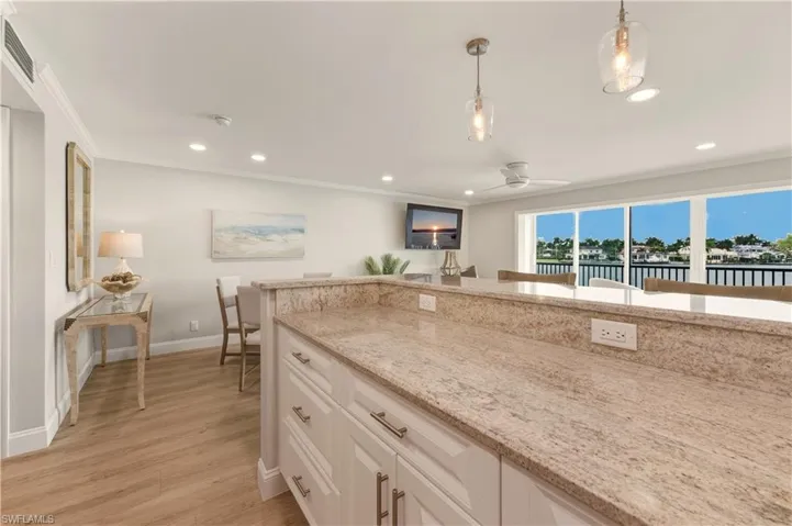 Kitchen with light stone countertops, pendant lighting, white cabinetry, light vinyl floors, and ornamental molding