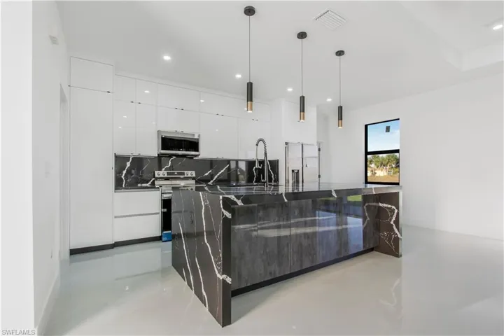 Kitchen with modern cabinets, a sink, white cabinetry, appliances with stainless steel finishes, and decorative backsplash