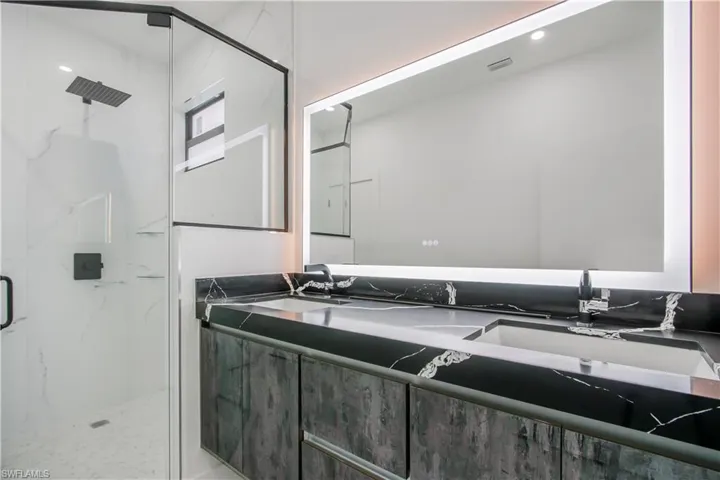 Full bath with double vanity, a marble finish shower, and visible vents