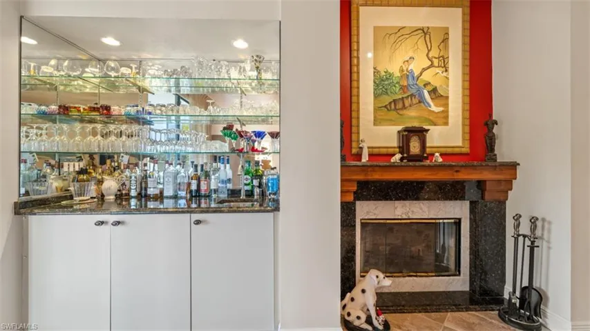 Indoor bar with white cabinets, a fireplace, dark stone counters, and recessed lighting