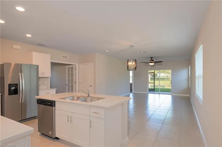Kitchen featuring appliances with stainless steel finishes, light tile patterned floors, light countertops, a kitchen island with sink, and white cabinets