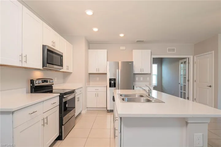 Kitchen featuring appliances with stainless steel finishes, an island with sink, light tile patterned flooring, recessed lighting, and white cabinetry