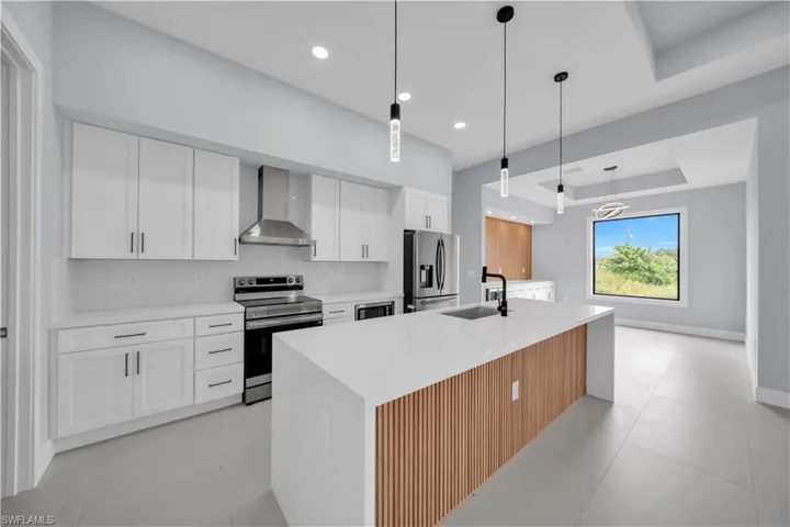 White cabinetry with stainless steel appliances, a large center island with wood-finish paneling, and pendant lighting