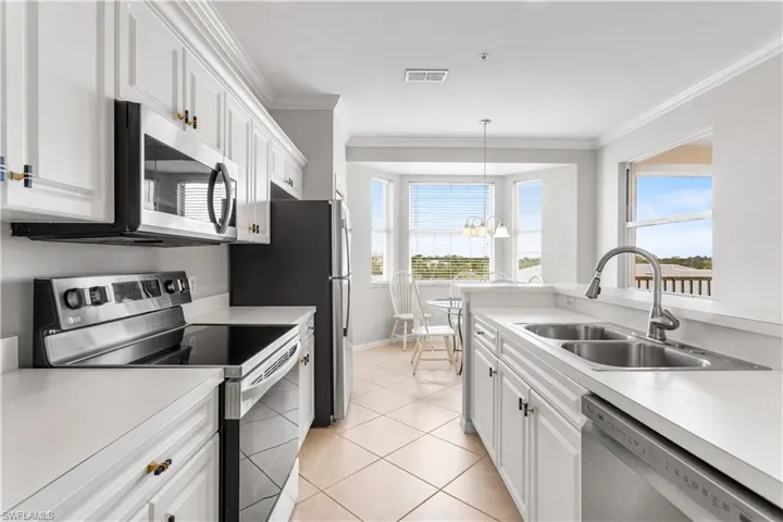 Kitchen with hanging light fixtures, appliances with stainless steel finishes, white cabinets, sink, and light tile floors