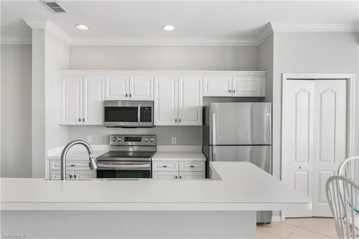 Kitchen with crown molding, light tile floors, white cabinets, and appliances with stainless steel finishes