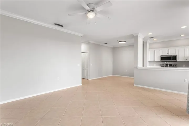 Unfurnished living room featuring sink, ceiling fan, light tile floors, and crown molding