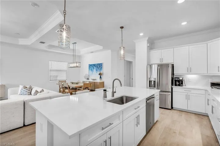 Kitchen with light wood-type flooring, an island with sink, sink, a tray ceiling, and appliances with stainless steel finishes