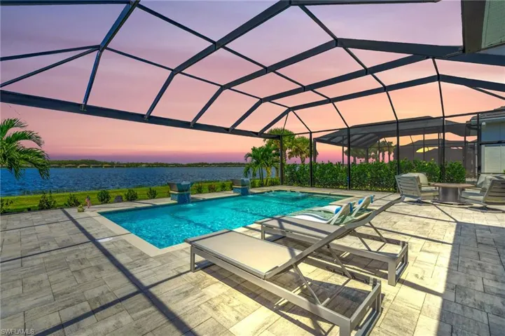 Pool at dusk with glass enclosure, a patio, and a water view