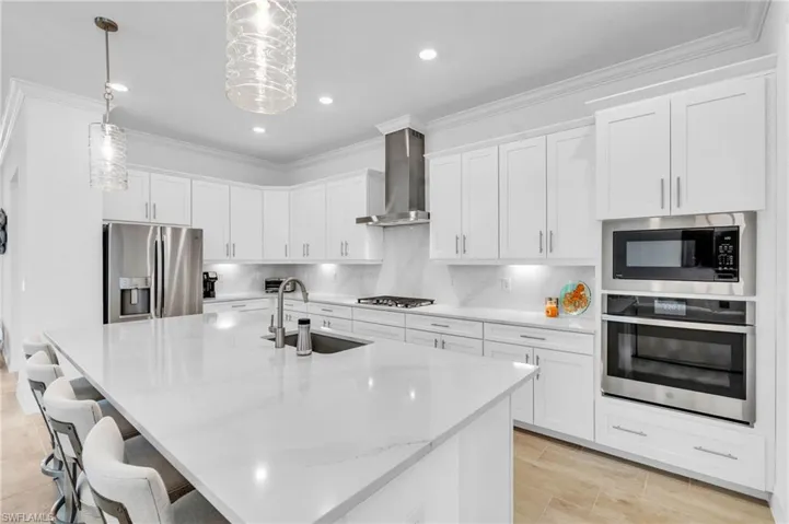 Kitchen with appliances with stainless steel finishes, hanging light fixtures, sink, wall chimney range hood, and white cabinets
