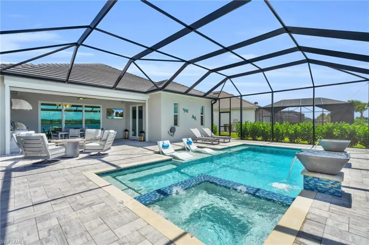 View of pool with glass enclosure, pool water feature, a patio area, and an in ground hot tub
