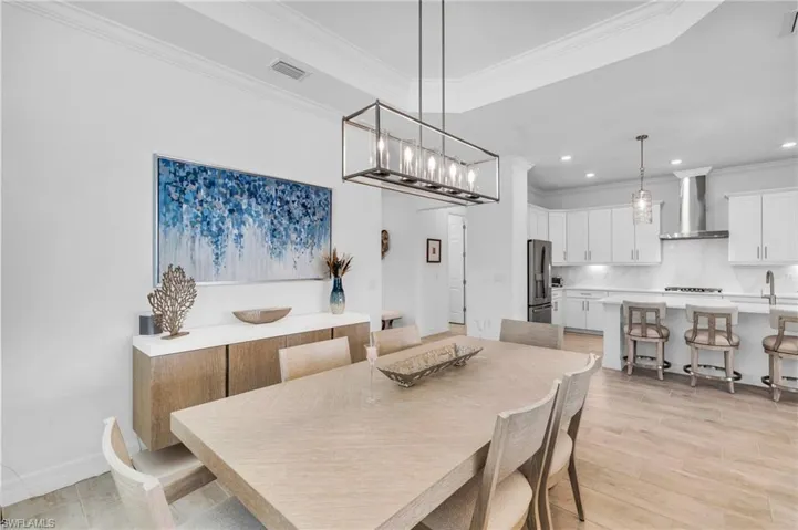 Dining space with light wood-type flooring, a tray ceiling, a notable chandelier, and ornamental molding