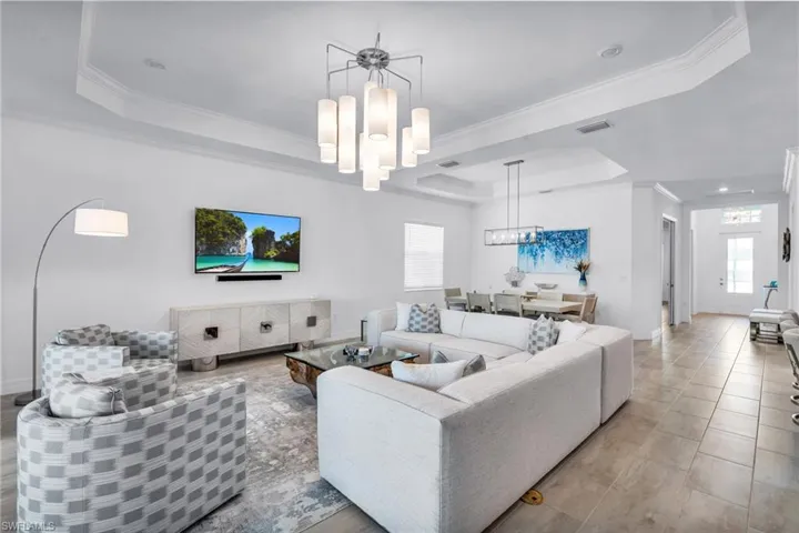 Living room featuring a tray ceiling, ornamental molding, plenty of natural light, and an inviting chandelier