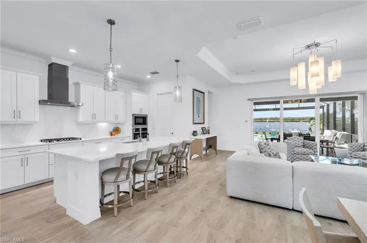 Kitchen featuring wall chimney exhaust hood, appliances with stainless steel finishes, a kitchen island with sink, a breakfast bar, and white cabinets
