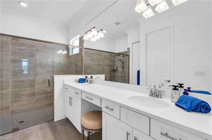 Bathroom with a shower with shower door, tile patterned flooring, crown molding, and vanity