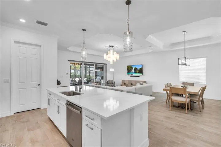 Kitchen featuring a kitchen island with sink, sink, hanging light fixtures, stainless steel dishwasher, and white cabinets