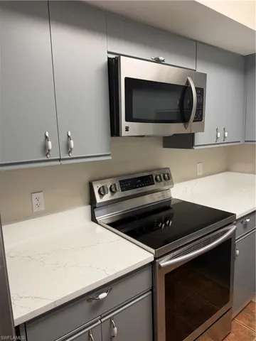 Kitchen featuring gray cabinets, stainless steel appliances, and light stone counters