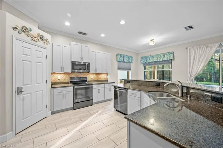 Kitchen with dark stone counters, white cabinets, sink, ornamental molding, and appliances with stainless steel finishes