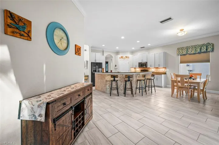 Kitchen featuring a center island, white cabinets, ornamental molding, black fridge with ice dispenser, and a breakfast bar area