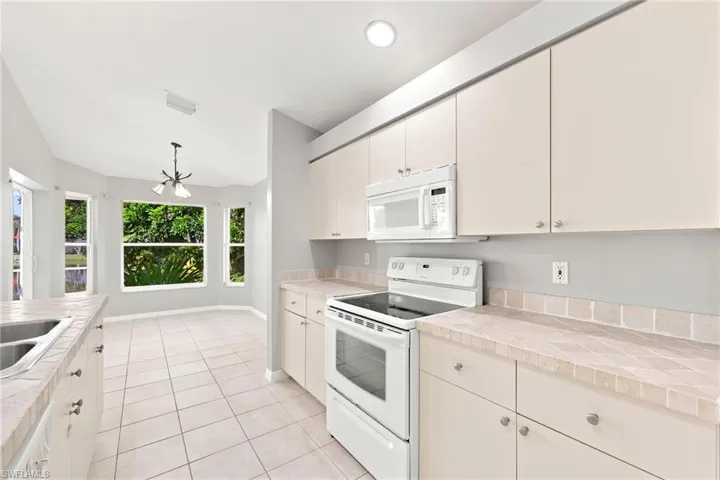 Kitchen featuring white appliances, cream cabinetry with brushed nickel hardware, and tile countertops