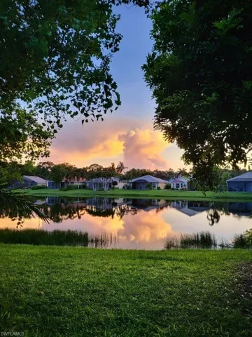 Expansive green lawn bordering a tranquil body of water, reflecting the colorful sky and distant residential structures