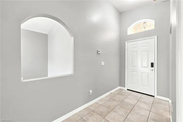 Entryway featuring light-toned tile flooring, a paneled white door with smart lock, and an arched transom window