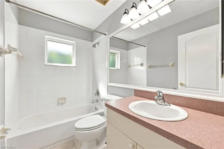 Full bathroom featuring a single vanity with a countertop and undermount sink, a large wall-mounted mirror, and a combined shower and tub with white tile surround