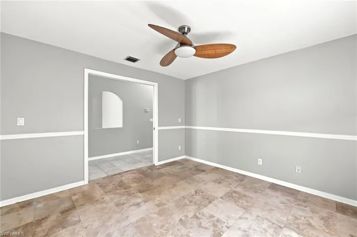 Spacious room featuring neutral wall tones with decorative chair rail molding, large format tile flooring, and a ceiling fan with integrated lighting