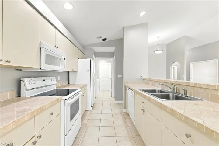 Galley kitchen featuring light cabinetry, tile flooring, white appliances, recessed lighting, and a double basin stainless steel sink
