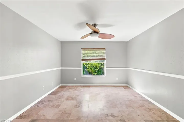 Spacious room featuring neutral grey walls with chair rail molding, a ceiling fan with integrated lighting, and tile flooring