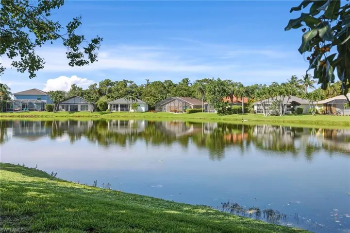 Expansive lakefront property featuring a serene water body, lush green landscaping, and mature tropical foliage