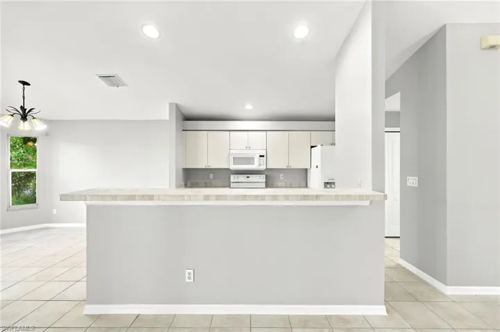 Kitchen featuring light cabinetry, a white microwave, and an electric range, complemented by a tiled backsplash