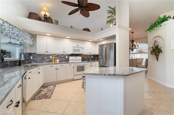 Kitchen featuring ceiling fan with notable chandelier, light tile patterned floors, a center island, appliances with stainless steel finishes, and decorative backsplash