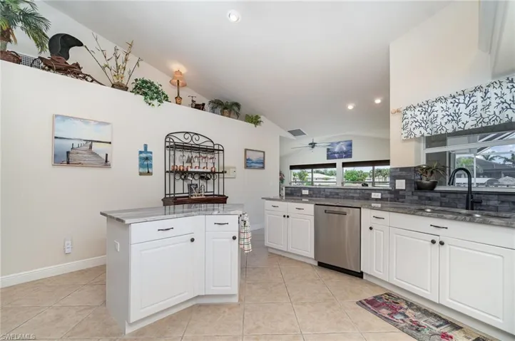 Kitchen featuring tasteful backsplash, dishwasher, a sink, light tile patterned flooring, and lofted ceiling