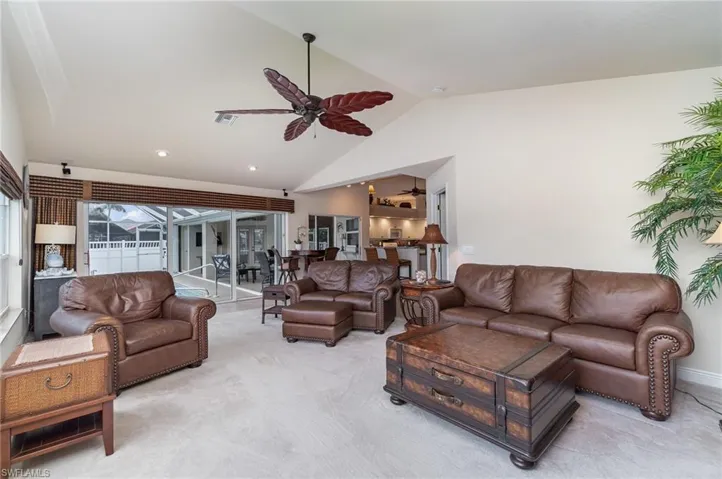 Living area with high vaulted ceiling, visible vents, light colored carpet, and a ceiling fan