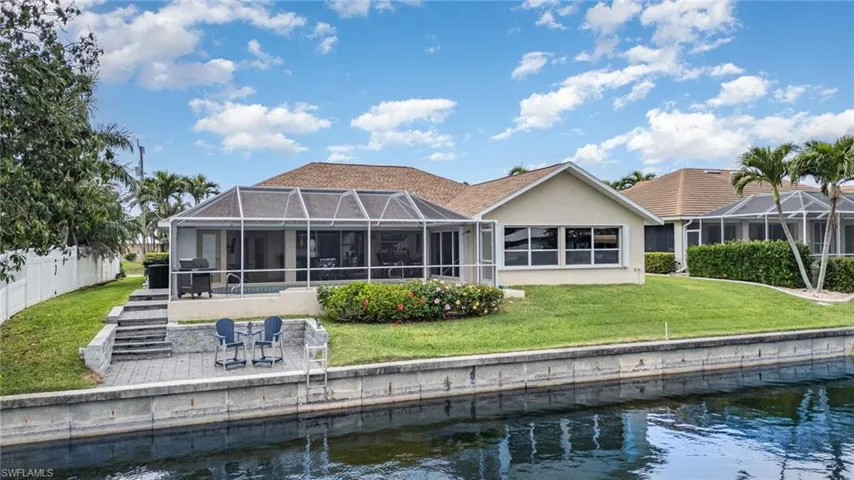 Back of house with stucco siding, glass enclosure, a water view, a patio, and fence