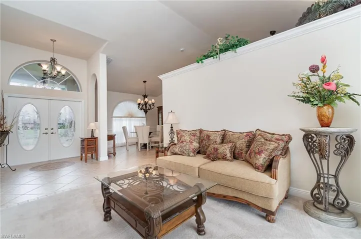 Living room with french doors, an inviting chandelier, tile patterned flooring, and high vaulted ceiling
