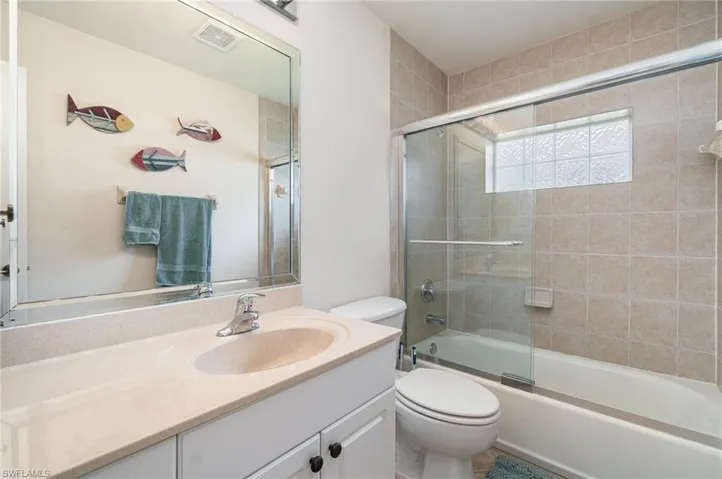 Bathroom featuring visible vents, toilet, vanity, and shower / bath combination with glass door