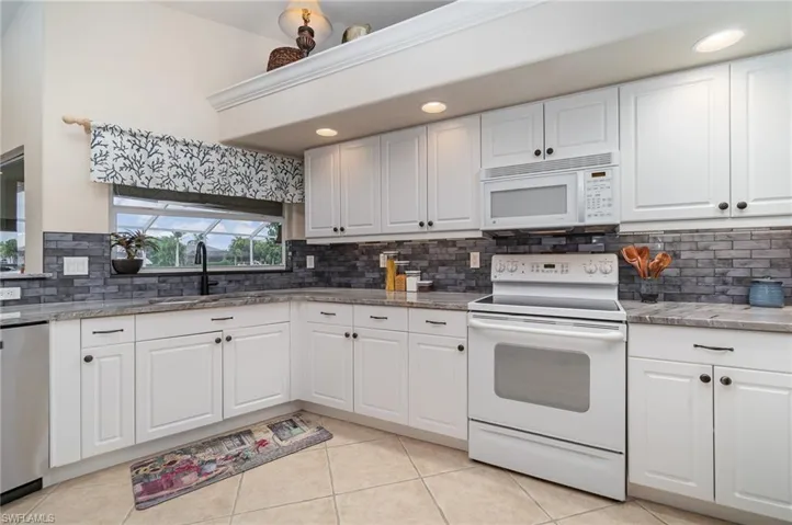 Kitchen featuring a sink, light tile patterned floors, decorative backsplash, and white appliances