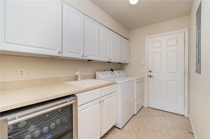 Laundry area featuring light tile patterned floors, baseboards, a sink, wine cooler, and washing machine and dryer
