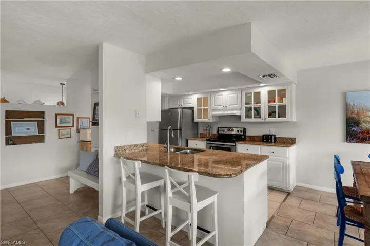 Kitchen featuring white cabinets, a breakfast bar, glass insert cabinets, light tile patterned floors, and a textured ceiling