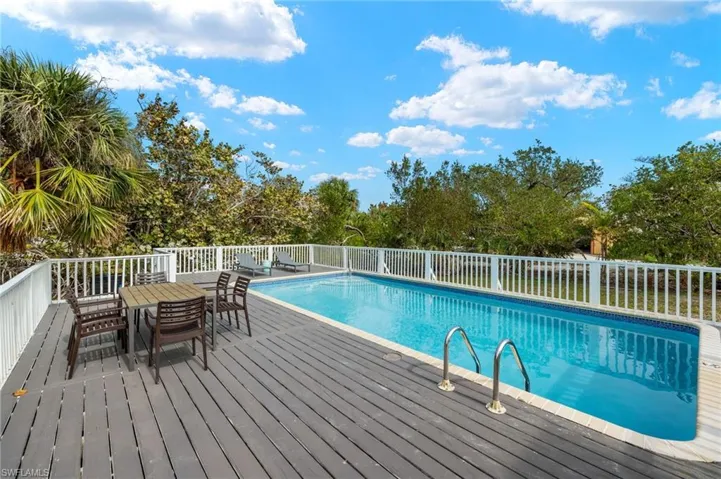 View of pool with outdoor dining area, view of scattered trees, and a wooden deck