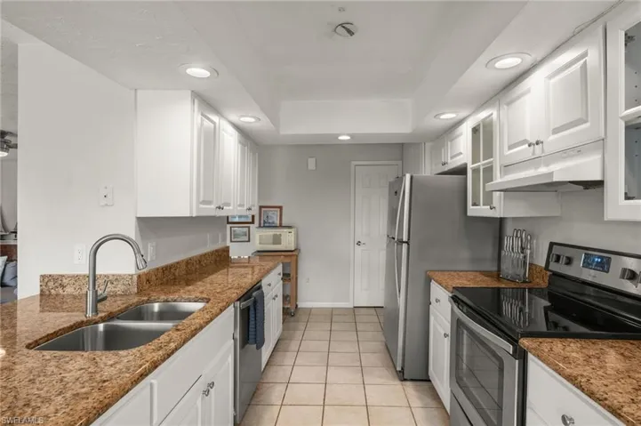 Kitchen featuring appliances with stainless steel finishes, white cabinetry, under cabinet range hood, recessed lighting, and dark stone countertops