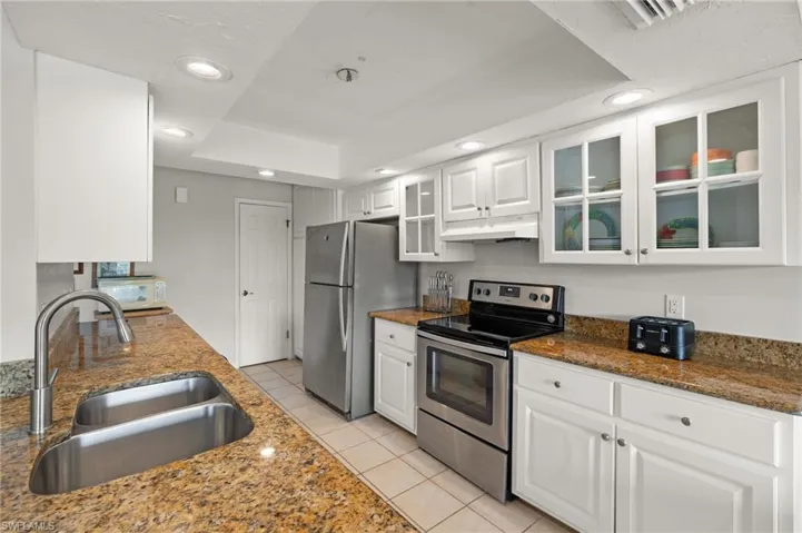 Kitchen with appliances with stainless steel finishes, white cabinets, light tile patterned floors, glass insert cabinets, and recessed lighting