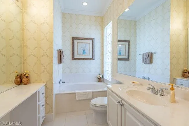 Bathroom with tile patterned floors, a healthy amount of sunlight, toilet, a washtub, and crown molding