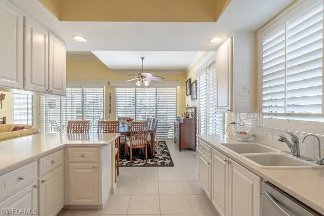 Kitchen with white cabinetry, ceiling fan, light tile patterned flooring, stainless steel dishwasher, and sink