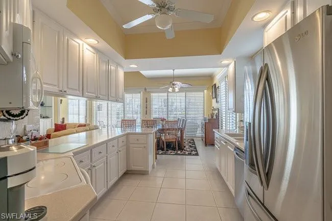 Kitchen featuring light tile patterned floors, white cabinetry, kitchen peninsula, stainless steel appliances, and a raised ceiling